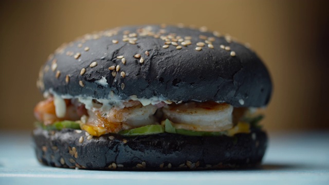用慢镜头将美味的黑色海鲜汉堡和虾、融化的奶酪、生菜和蔬菜放在桌子上。黑色的汉堡面包，压缩后的原始形状。视频素材