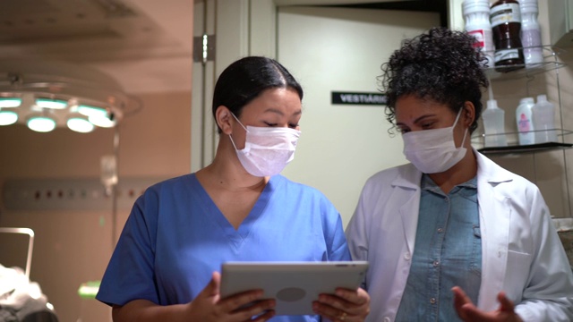 医疗工作者在医院带着口罩行走和使用数字平板电脑视频素材