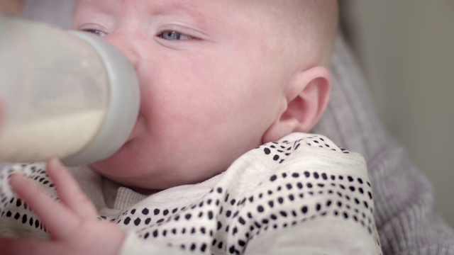 可爱的蓝眼睛的小男孩喝婴儿奶瓶由母亲抱着，在家里微笑视频素材