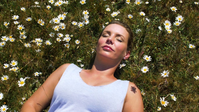 一个女人平静地躺在雏菊丛中。花儿在微风中摇曳。视频素材