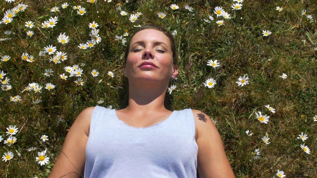 一个女人平静地躺在雏菊丛中。花儿在微风中摇曳。视频素材