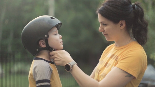母亲在调整小儿子头上的自行车安全帽。视频素材