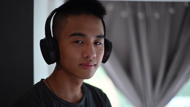一个亚洲的中国少年在听音乐，他的耳机看着相机手臂交叉视频素材