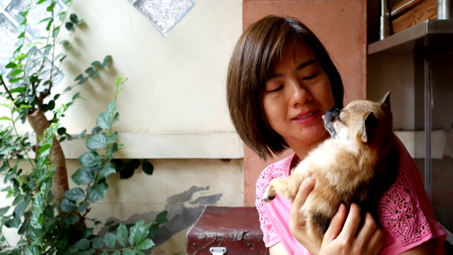 短发亚洲女人抱着一只狗在房子前玩耍视频下载