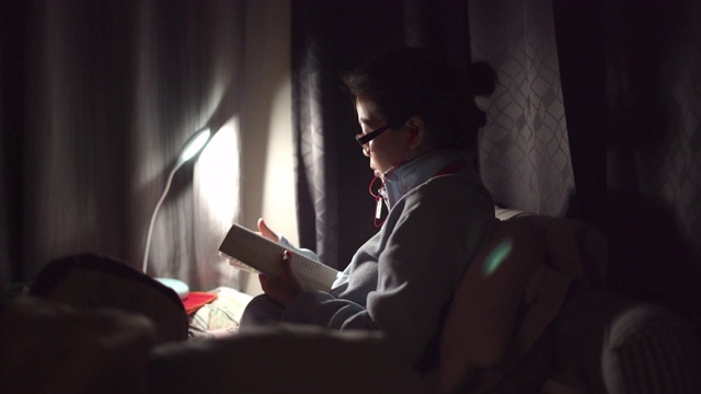 一个亚洲女人晚上在床上看书视频素材
