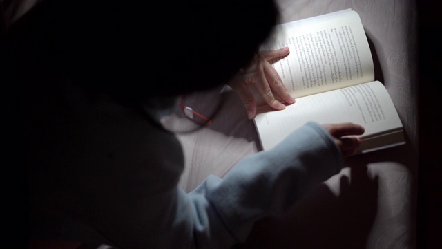一个亚洲女人晚上在床上看书视频素材