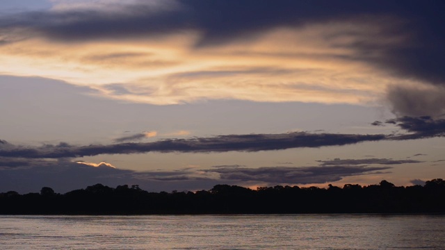 树木的剪影和平静的亚马逊河在一个辉煌的日落风景在秘鲁的戏剧性的天空下-广角拍摄视频下载