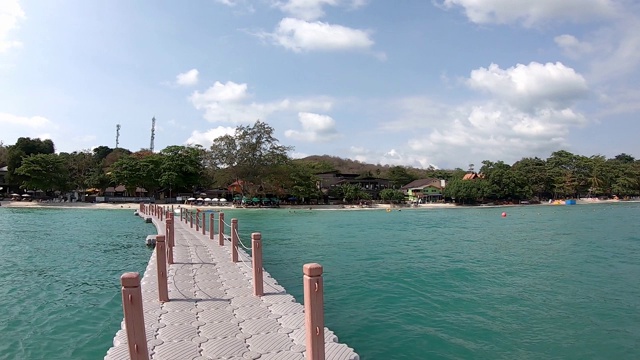 视频从右边移动到左边的渔船和浮动码头的塑料，根据海浪的背景海滩和山在泰国罗永koh Samet的旺堤海滩。视频下载