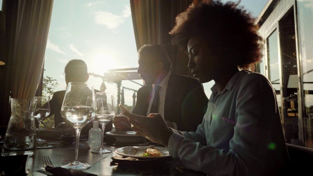 优雅的非裔美国女商人在和同事吃商务午餐时看手机上的电子邮件视频素材