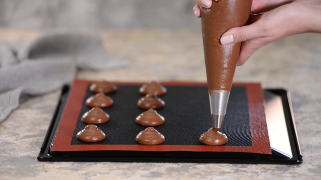 烹饪巧克力卷时，女性用手把面团从袋子里挤到烤盘上视频素材