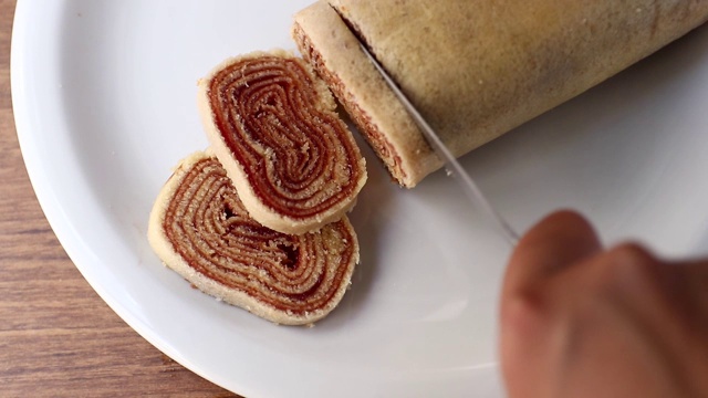在切罗洛之火。将巴西甜点Bolo de Rolo(瑞士卷，卷饼)切成薄片，放在白色的盘子上，以木材为背景视频素材