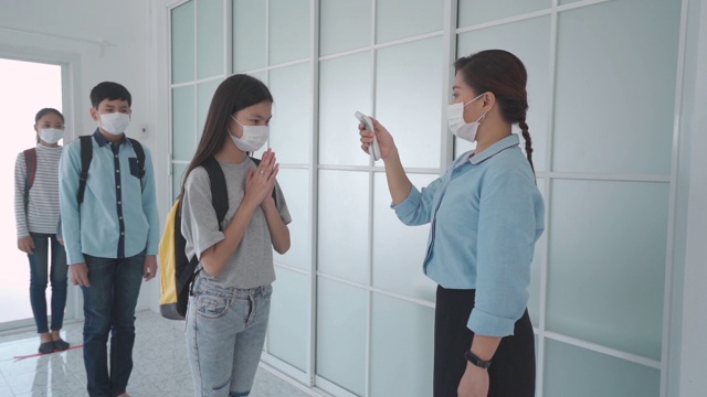 亚洲女教师在学生返校时使用体温计检查学生体温，以防止COVID-19的传播，新常态和教育理念。视频下载