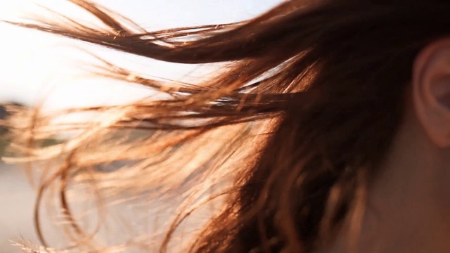 近后视图棕色女人的头发柔嫩的运动在空气中的慢动作120帧/秒。黑发女人戴着墨镜走在沙滩上。风吹着轻盈的头发在夕阳下闪闪发光。宏观的视频视频素材