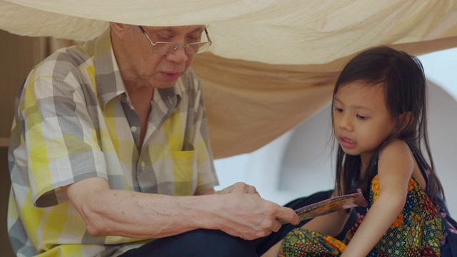 老男人和女孩在客厅里的自制营地里看书视频下载