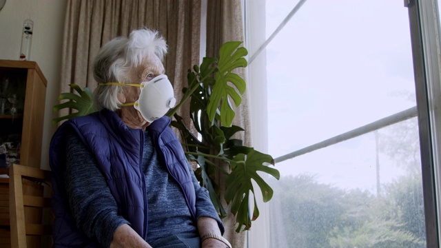 广角拍摄悲情的白种老年妇女戴着n95防护口罩望着窗外感到孤独预防COVID SARS nCoV 19冠状病毒猪流感H7N9流感疾病在寒冷和流感季节视频下载
