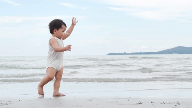 快乐的亚洲小男孩儿子学习走在热带海滩上有乐趣沿着边缘的日落海浪在沙滩上。视频下载