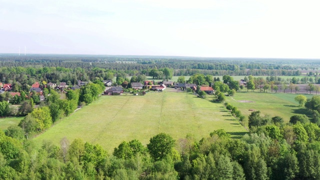 鸟瞰图一排树和一个草地在村庄的边缘与村民的房子在背景。视频素材