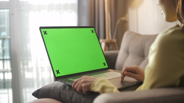 亚洲妇女坐在沙发上使用绿色屏幕的笔记本电脑视频下载
