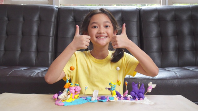 亚洲女孩在家的时候在客厅里展示造型粘土和工艺品。她把五颜六色的橡皮泥塑造好，把自己想象出来的玩具艺术品放在桌上。艺术和工艺概念。视频下载