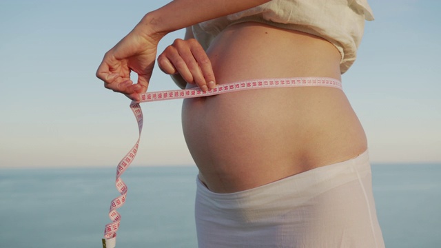 年轻女性在测量她怀孕期间的肚子还多大。视频素材