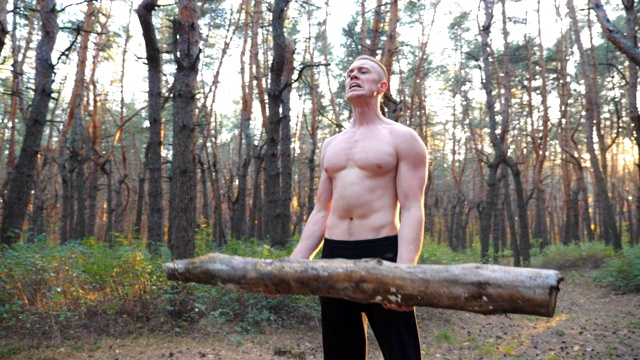 肌肉发达的男子举起了负重训练的二头肌。强壮强壮的家伙在日落时分在森林里工作。使用大圆木进行户外运动的运动员。运动和积极的生活方式的概念。多莉拍摄视频下载