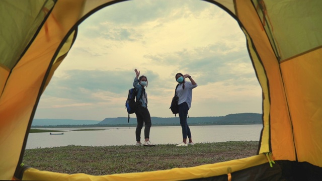 两个亚洲女背包客戴着面罩在湖边欣赏夏日日落的慢镜头。他们是快乐的，有乐趣的假期，放松的时刻。青少年自然户外日常生活的概念视频素材