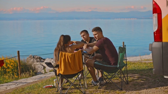 一群年轻的朋友在露营地用餐。朋友享受大海。视频下载