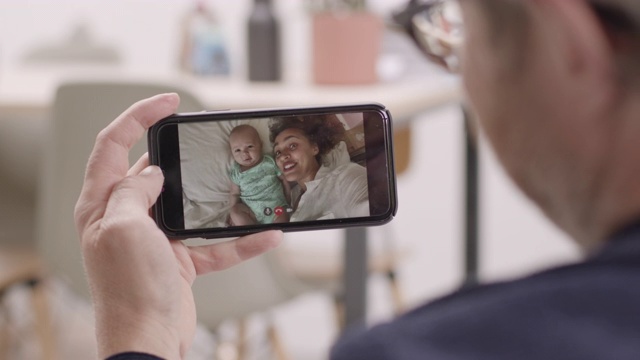 真实的近距离的年轻的成年母亲和她的新生儿在床上做视频电话给家人亲戚在沙发上使用智能手机视频素材