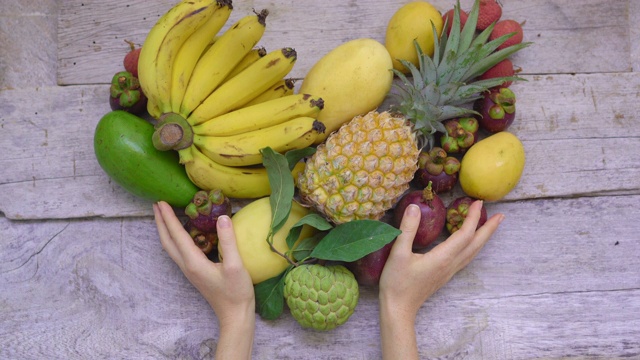 顶部的观点-一个女人的手握着一颗由许多热带水果制成的心视频下载