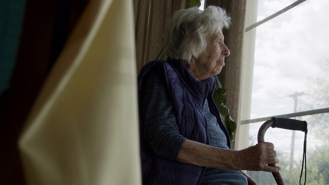 广角揭示一个快乐的，舒适的老年白人妇女在夏天看窗外的照片视频素材