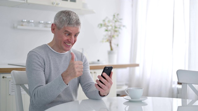 一位老人在家里庆祝智能手机的成功视频素材