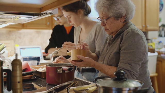 奶奶在炉子上的锅里放盐，她的两个孙女也在做饭。视频下载