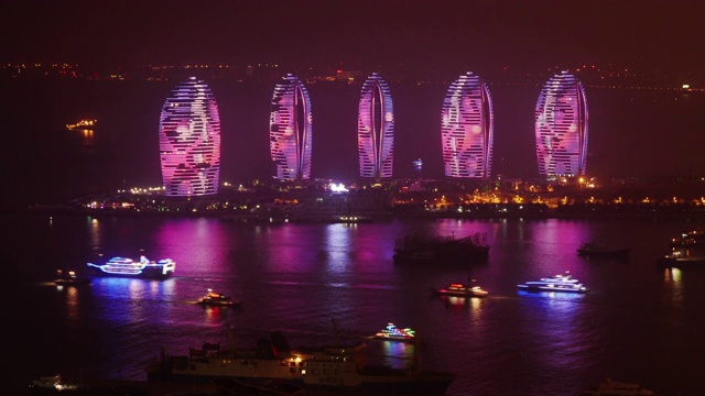 在中国海南省三亚市的凤凰岛上，未来主义的灯光摩天大楼的夜晚时光流逝。中等宽的视野从上面视频下载