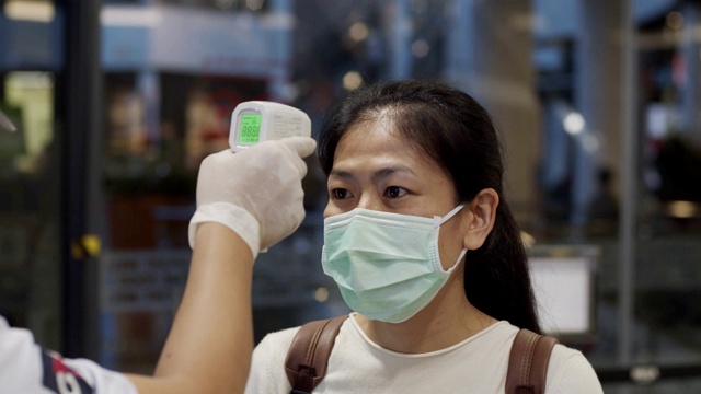 一名亚洲女子进入商场前正在接受体温检查。视频素材