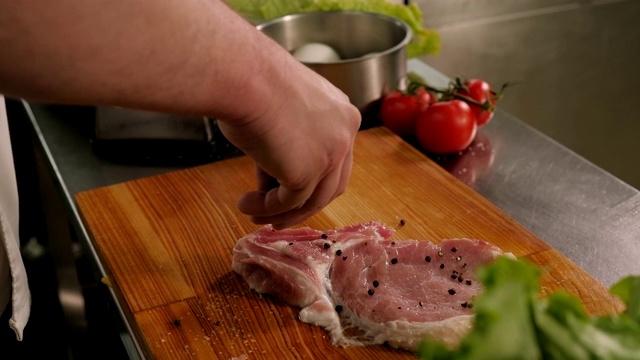 男厨师将新鲜猪肉牛排和胡椒洒在切菜板上的特写镜头视频下载