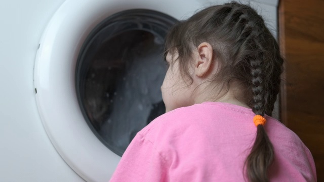 一个小女孩看着一台工作的洗衣机。视频下载