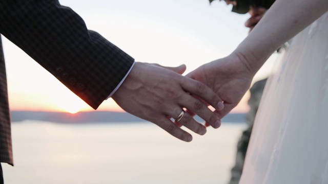 新婚夫妇在日落时牵手。阳光透过他们的手指照射下来。爱情、幸福和友谊。日出时双手合拢。视频下载
