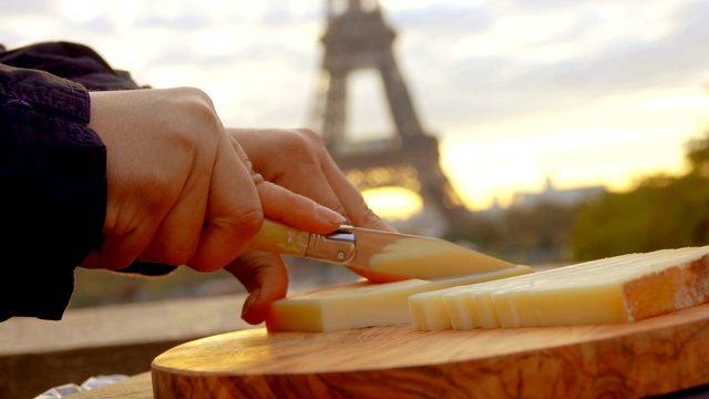 手在埃菲尔铁塔的背景下用刀切硬山羊奶酪视频下载
