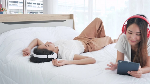 亚洲十几岁的女孩在床上使用数字平板电脑耳机快乐视频素材