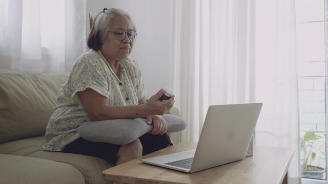 老年女性患者在家中用笔记本电脑与医生视频聊天，讨论如何服药。视频素材