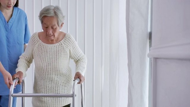 亚洲女护士医生，帮助82岁的亚洲老年妇女在家或医院步行训练和康复过程。老祖母倾听照顾者给予的支持，老年人医疗保健，物理治疗。在家里照顾者视频下载