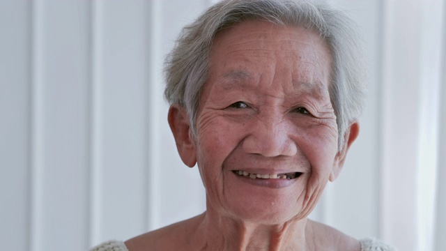 白发苍苍的老女人在家里看着照相机。快乐善良的老年妇女微笑，同时在一个伟大的心情。快乐的长者成熟的祖母与牙齿的微笑在家里或退休的房子视频下载