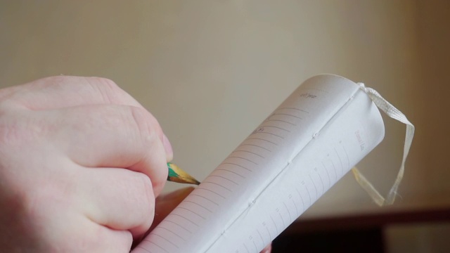 一个男性用铅笔在笔记本上写字的手的特写视频素材