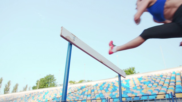 白人女运动员在体育场练习，在跑道上跨栏，慢动作。体育场内田径运动训练视频下载