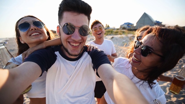 Pov的观点，年轻的朋友在日落的海滩上与饮料的乐趣自拍。在线视频通话:一名男子在热带岛屿上看着智能手机摄像头，一名女子在喝柠檬水，挥手致意视频素材