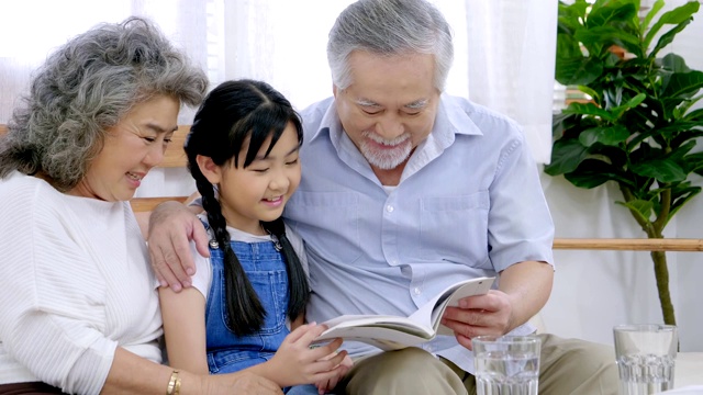在度假的房子的客厅里，亚洲的爷爷奶奶和孙女正在读着幸福的笑脸视频素材