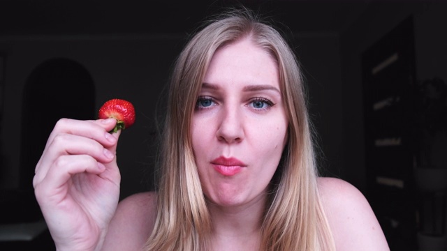 美丽的金发女人看着镜头吃着一个大的多汁的草莓，享受视频素材