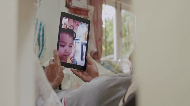 4k分辨率手持式拍摄亚洲高级男子在冠状病毒封锁情况下，手持平板设备与外孙女进行视频通话或视频会议技术交谈。视频素材