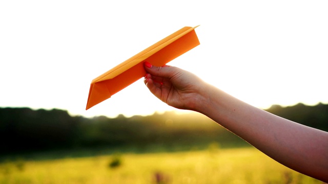 在橙色的夕阳下，一个女人手拿着纸飞机。自由的概念视频素材