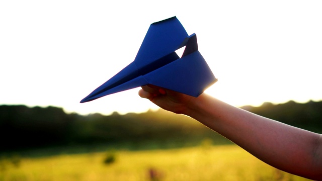 在橙色的夕阳下，女人手拿着蓝色的纸飞机。自由的概念视频素材